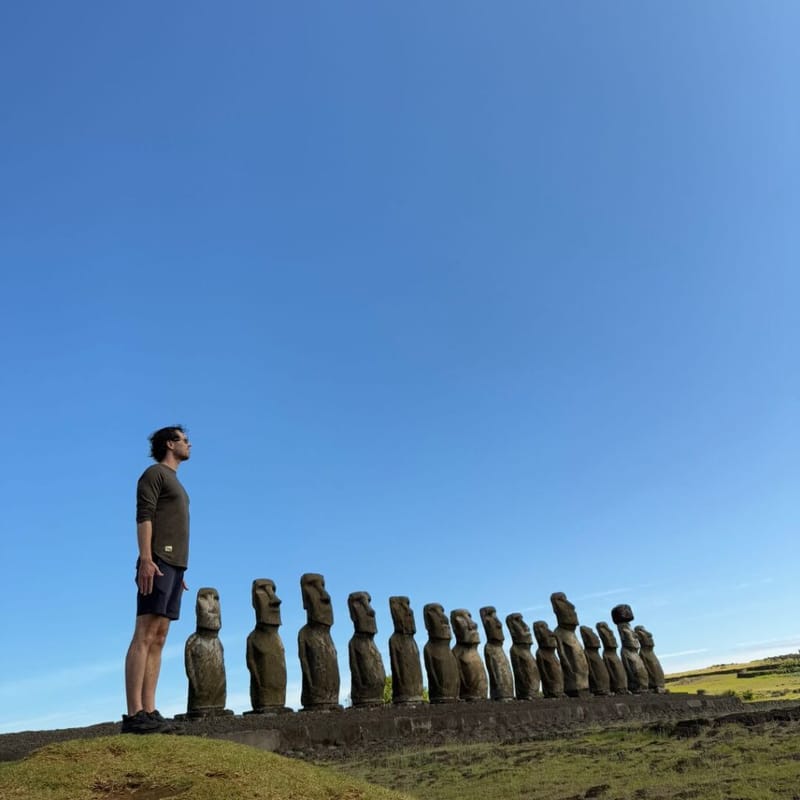 John Arrow standing beside a row of moai statues on Easter Island under a clear blue sky